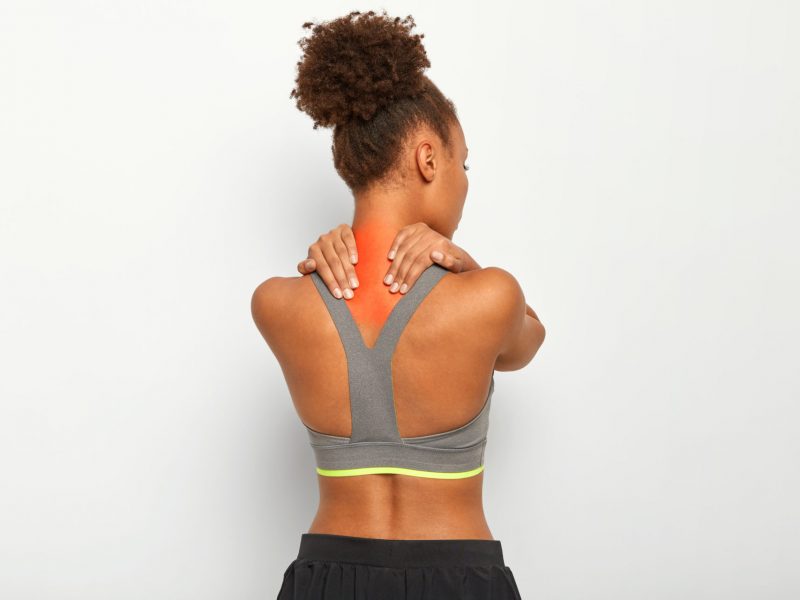 curly haired young afro woman massages tense muscles has pain neck spasm dark skin wears sport bra isolated white background